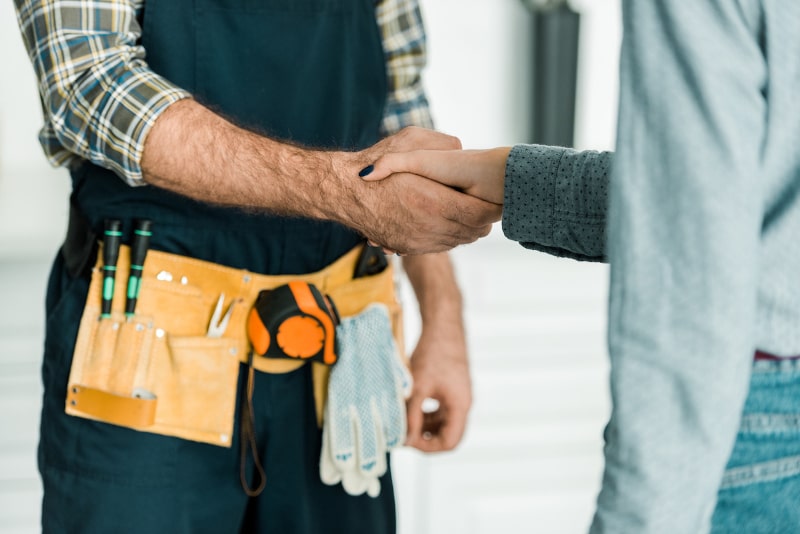torso shot of handshake between contractor wearing tool belt and client