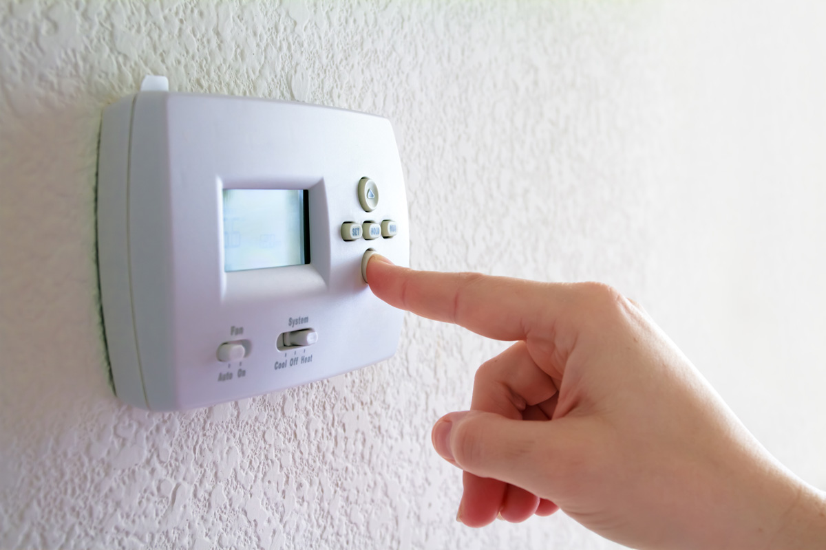 A person’s hand adjusting the temperature on a thermostat in El Paso.