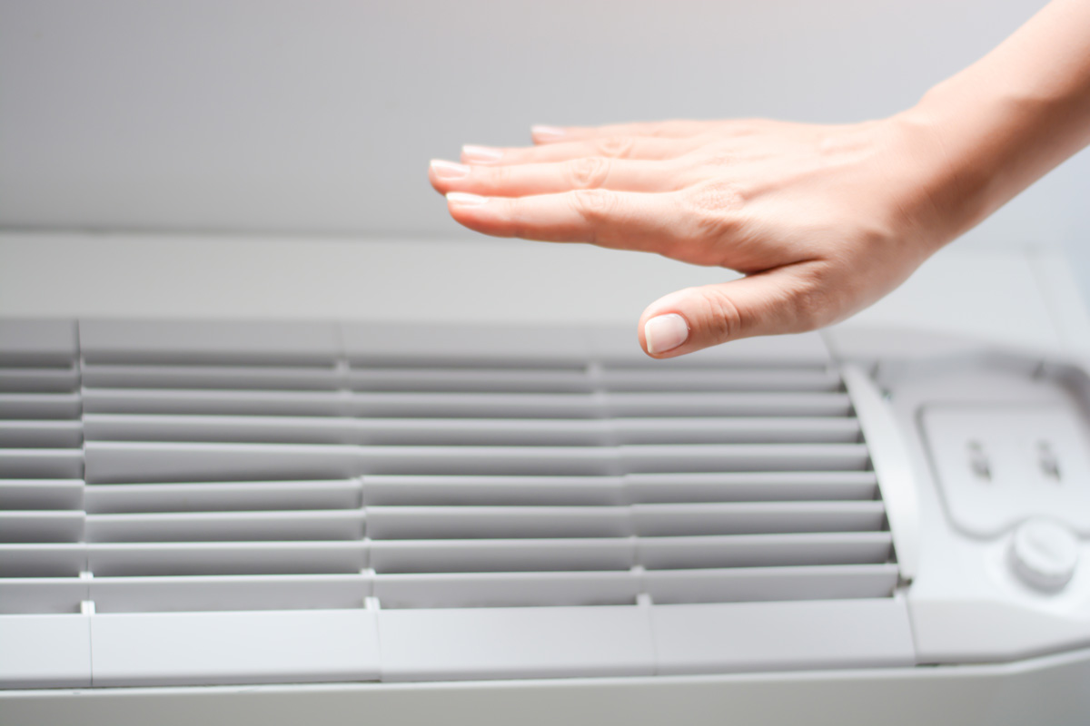 A person’s hand feeling air coming out of an air conditioning unit in an El Paso home.