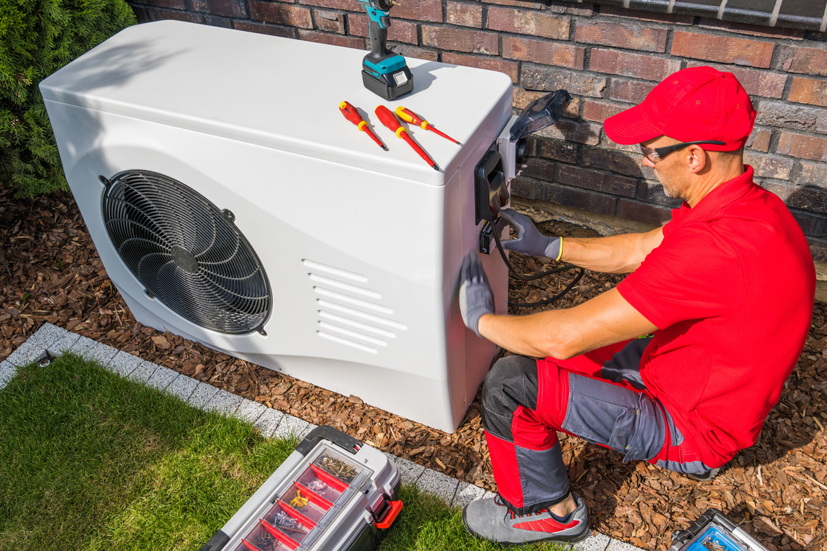 A man in a red hat and shirt performing air conditioning service on a white AC unit in El Paso.