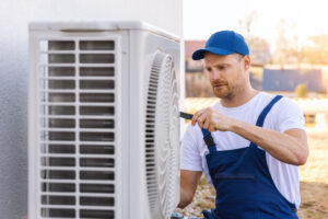 A man in a blue hat performing AC repair on an outdoor AC unit in El Paso.