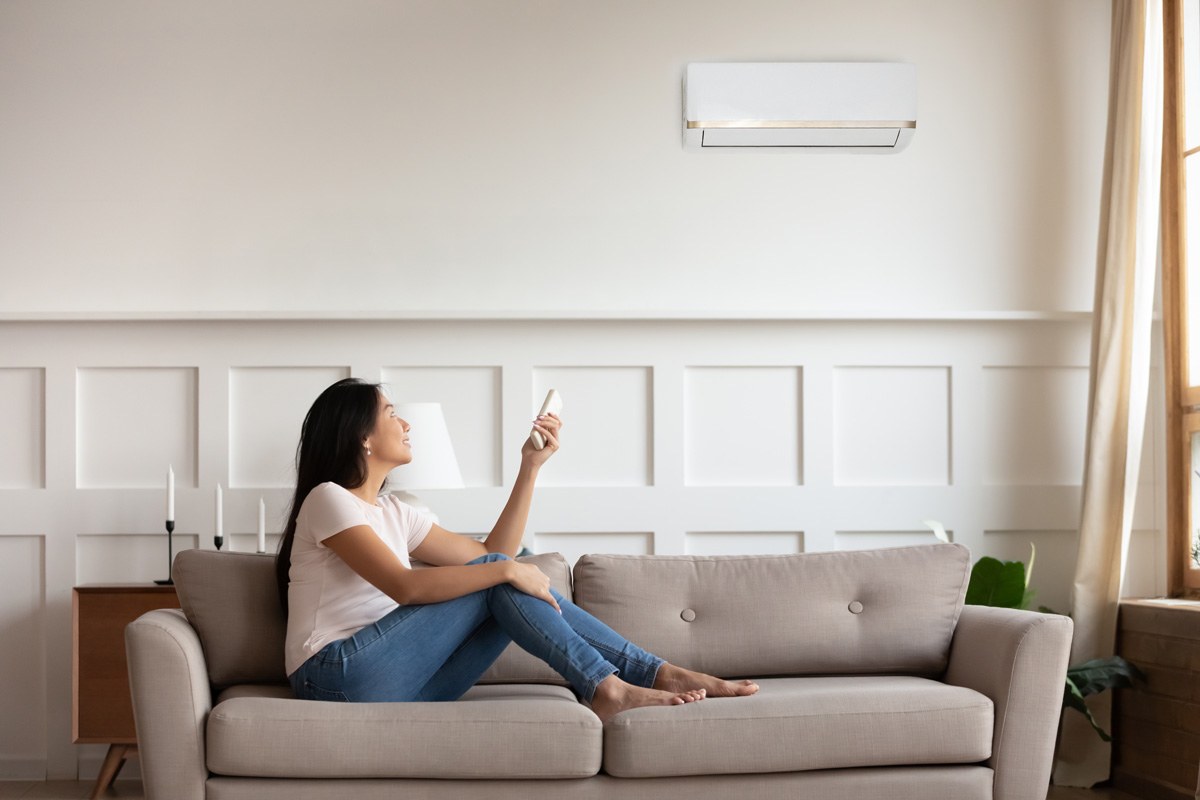 A woman sitting on a couch using a remote to turn on her wall-mounted HVAC unit in El Paso.